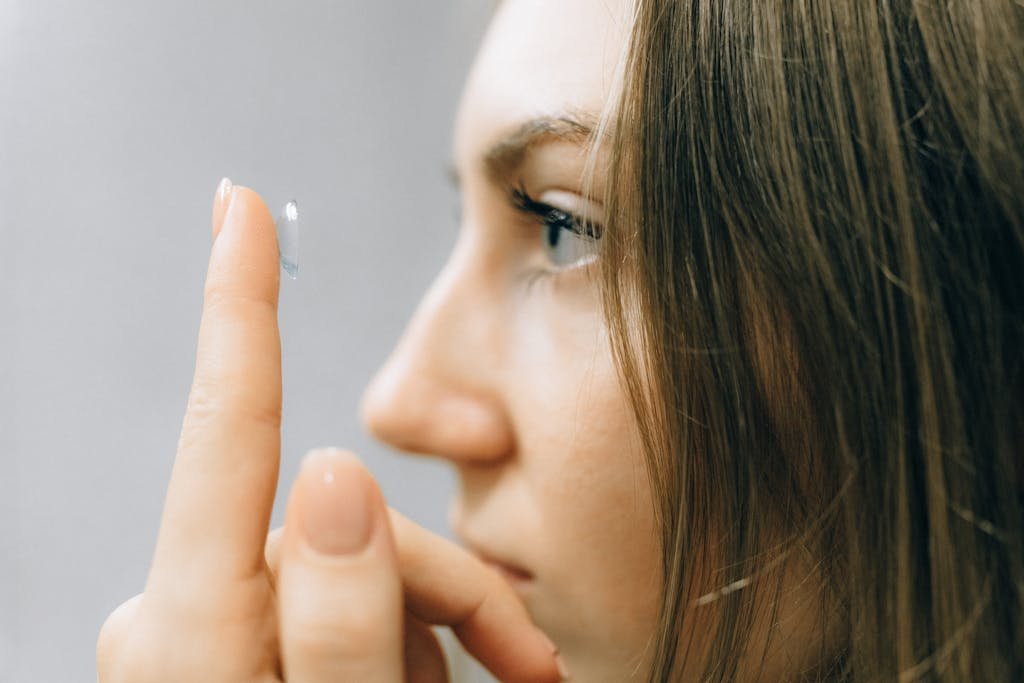 A young woman focuses intently as she applies a contact lens, close-up shot highlighting her eye and careful fingers.