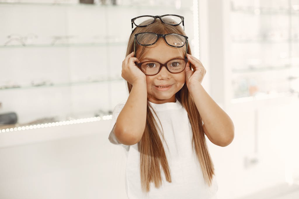 Cheerful girl trying on glasses in an optical shop, showcasing a fun eyewear selection process.