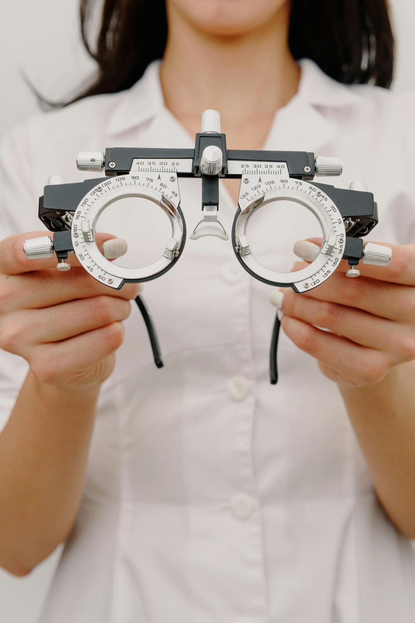 Crop anonymous female optometrist wearing white robe showing trial frame with optical lenses while working in contemporary ophthalmology center